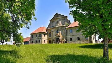 Ein historisches Steinhaus mit rotem Dach, umgeben von üppigem Grün und Bäumen.
