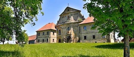 A historic stone building with a red roof, surrounded by lush green grass and trees.