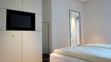 Ein Schlafzimmer mit einem Bett, einem an einer Kommode befestigten Fernseher und einem Spiegel an der Wand.