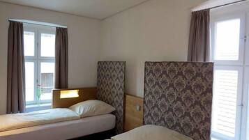 Ein Hotelzimmer mit zwei Betten, einem fensterbelaubten Fenster und einer Heizung.