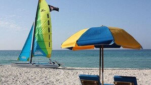 Una playa con un velero, una sombrilla y sillas de playa.