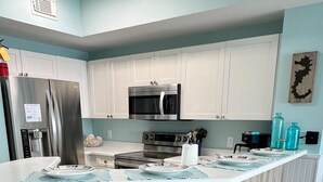 Una cocina moderna con armarios blancos, electrodomésticos de acero inoxidable y una isla central con taburetes de bar.