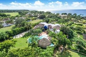 A resort with a swimming pool, thatched-roof structures, and a view of the ocean.