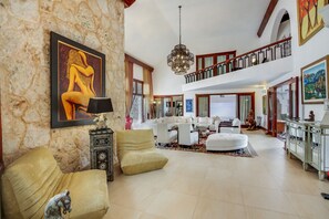 A spacious living area with a high ceiling, a chandelier, and a large painting on the wall.