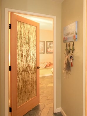 Een gang met een houten deur, een stenen vloer en een muur met een bord en decoratie.