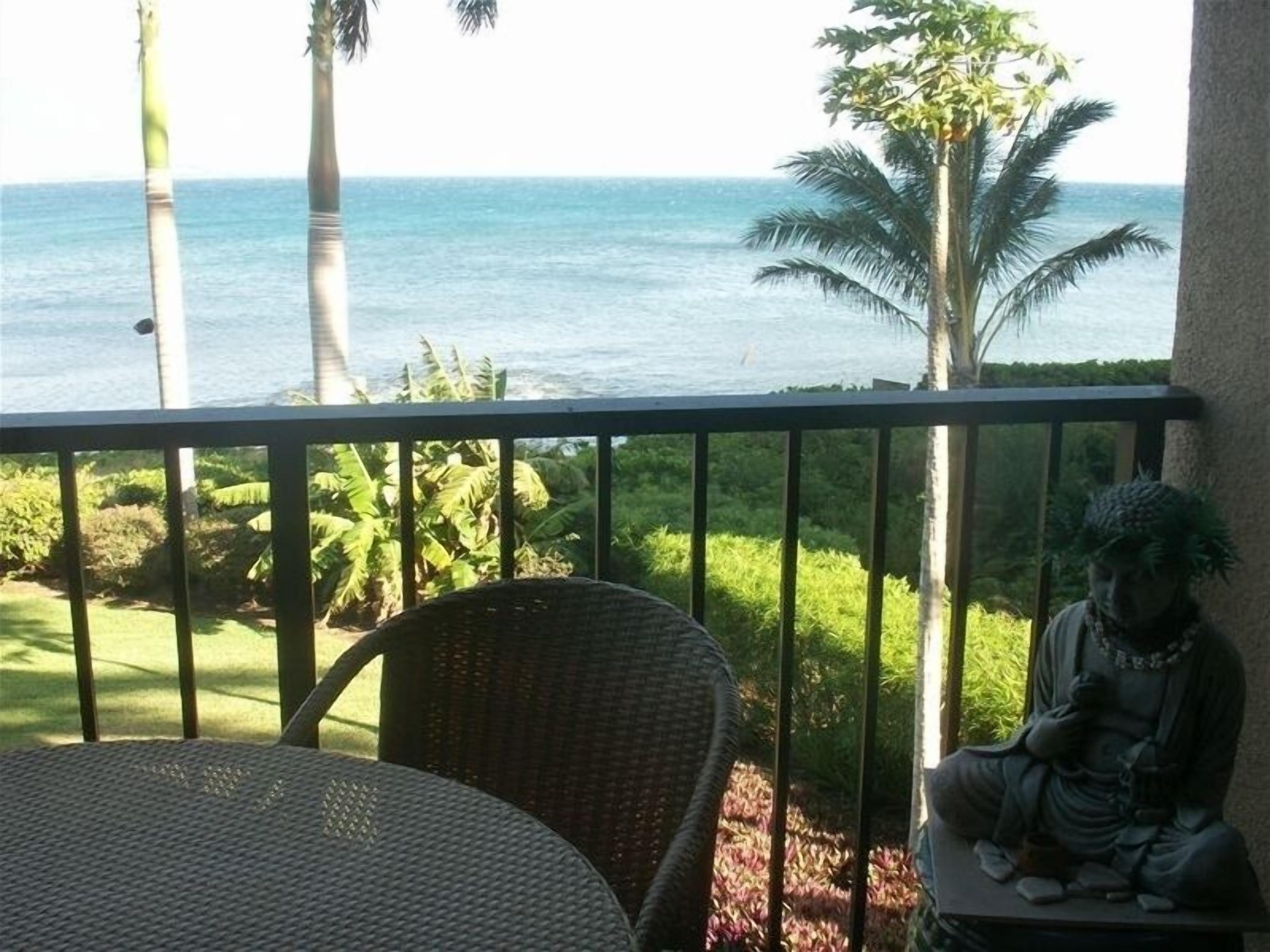 A balcony with a view of the ocean, a statue, and a wicker chair.