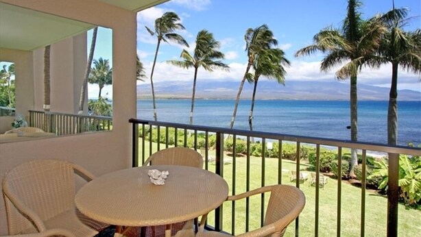 Un balcon meublé de mobilier en osier, donnant sur une plage bordée de palmiers et sur l’océan.