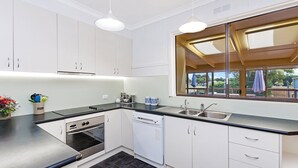 Ett modernt kök med vita skåp, en svart bänkskiva, en inbyggd ugn, en diskmaskin och ett stort fönster med utsikt över omgivningen.