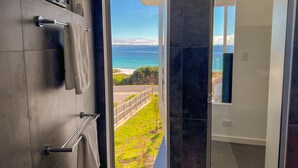 A bathroom with a view of a beach and ocean through a glass door.