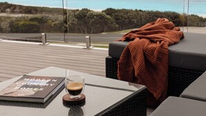 A modern outdoor seating area with a view of a lake, a book titled "Modern Country Homes," and a glass of coffee on a table.