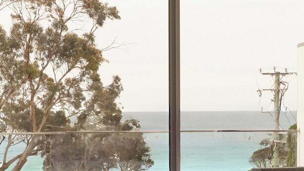 A bedroom with a large window overlooking a beach and a bridge.