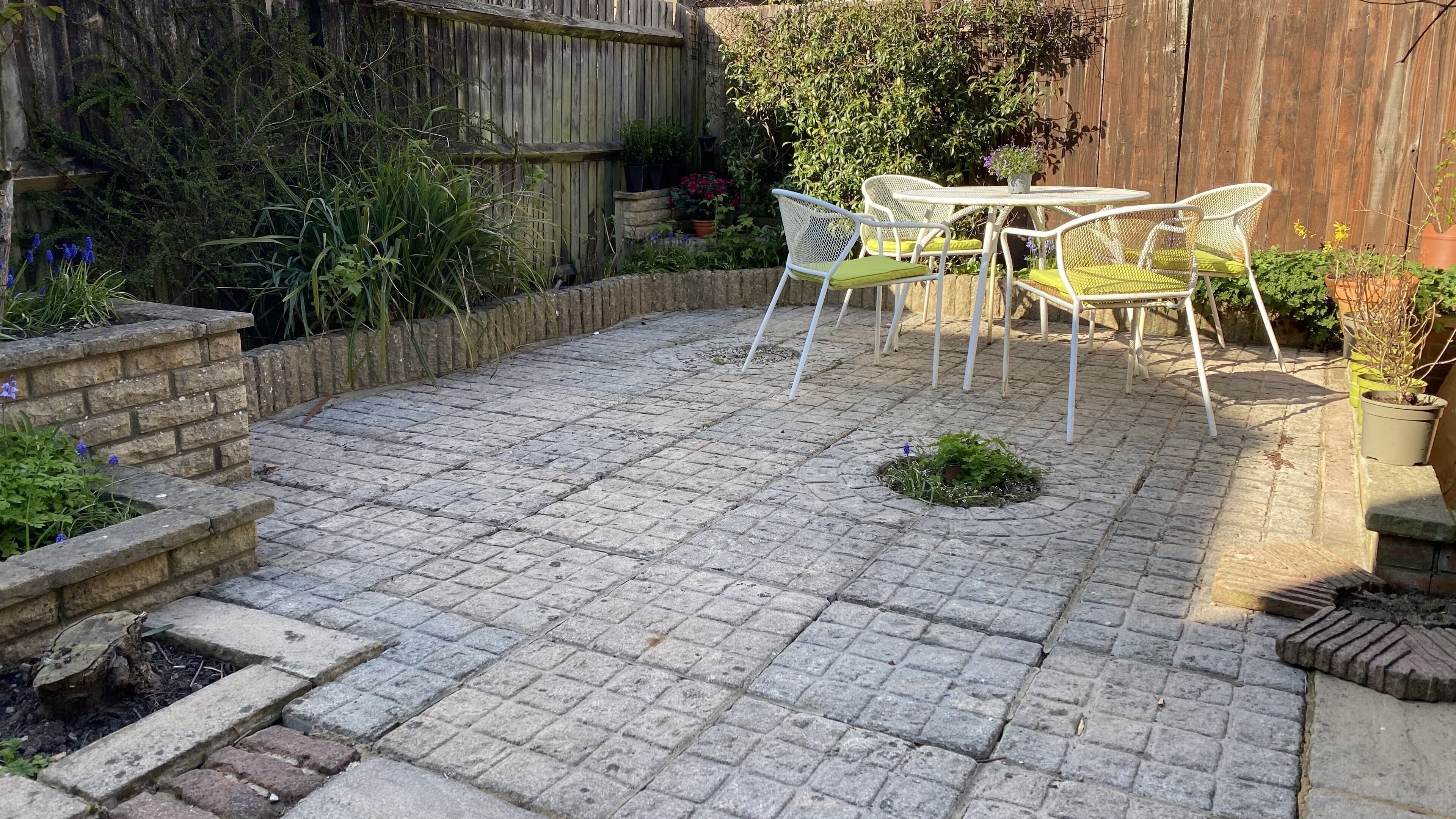 Een terras met stenen bestrating, witte metalen stoelen en potplanten.