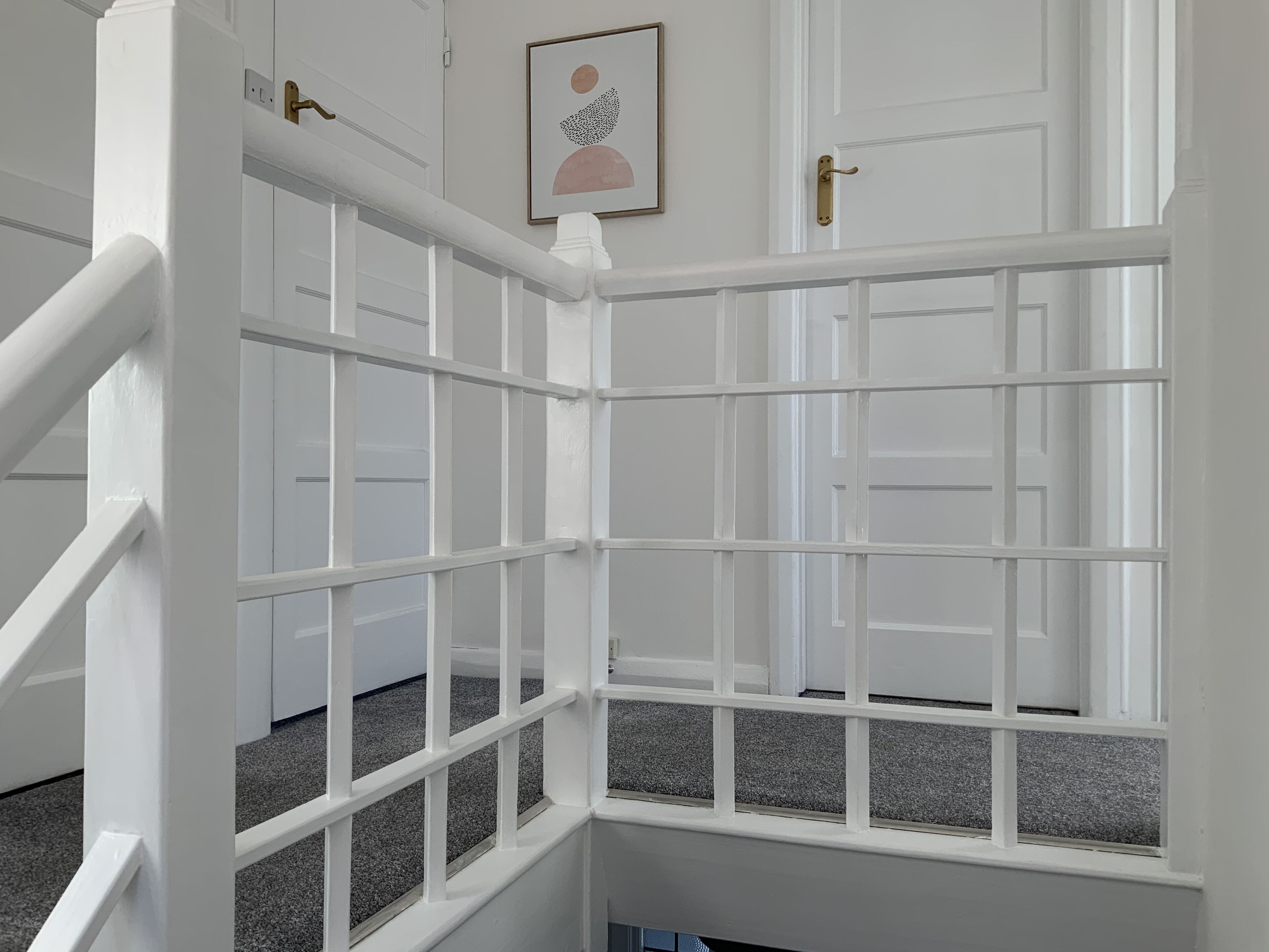 Una puerta blanca con un diseño de ventana enrejada, un pomo de latón y una obra de arte enmarcada encima.