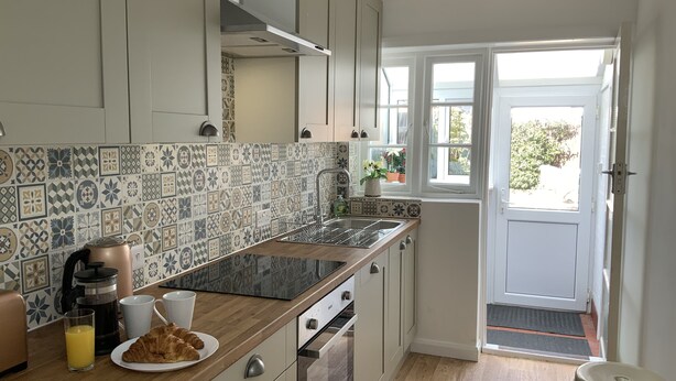 Cozinha com ladrilhos estampados, bancada de madeira e vista para o exterior através de uma porta.