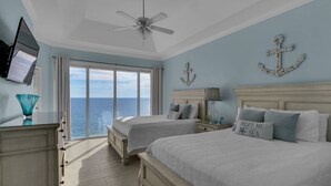 Un dormitorio con dos camas, un ventilador de techo, un televisor y vista al mar.