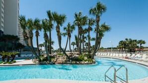 Una piscina con palmeras, sillas de descanso y un cielo azul despejado.