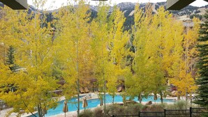 Zona de piscina rodeada de árboles con hojas amarillas, con una montaña al fondo.