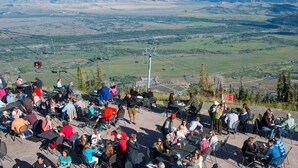 Un grupo de personas cenando al aire libre con una vista panorámica de montañas al fondo.