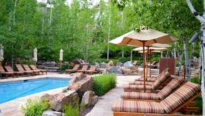 Zona junto a la piscina con sillones de descanso y sombrillas, rodeada de vegetación y jardines de piedra.