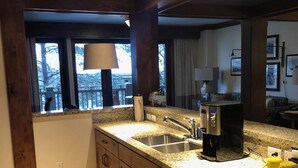 Una cocina con encimeras de granito, electrodomésticos de acero inoxidable, armarios de madera y una ventana con vista a árboles.