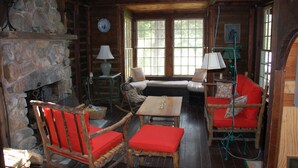L’intérieur d’un chalet rustique, avec une cheminée en pierre, des meubles en bois et de grandes fenêtres.