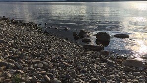 Une plage de galets, avec une eau calme et des montagnes lointaines sous un ciel nuageux.