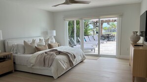 A bedroom with a bed, bedside tables, a ceiling fan, and a view of an outdoor patio with lounge chairs.