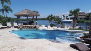 A pool area with lounge chairs, a thatched umbrella, and a view of the water.