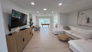 A modern living room with a flat-screen TV, a pool table, and a white sofa.