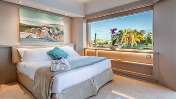 A modern bedroom with a large bed, a painting of seashells, a view of palm trees, and a window with a view of the outdoors.