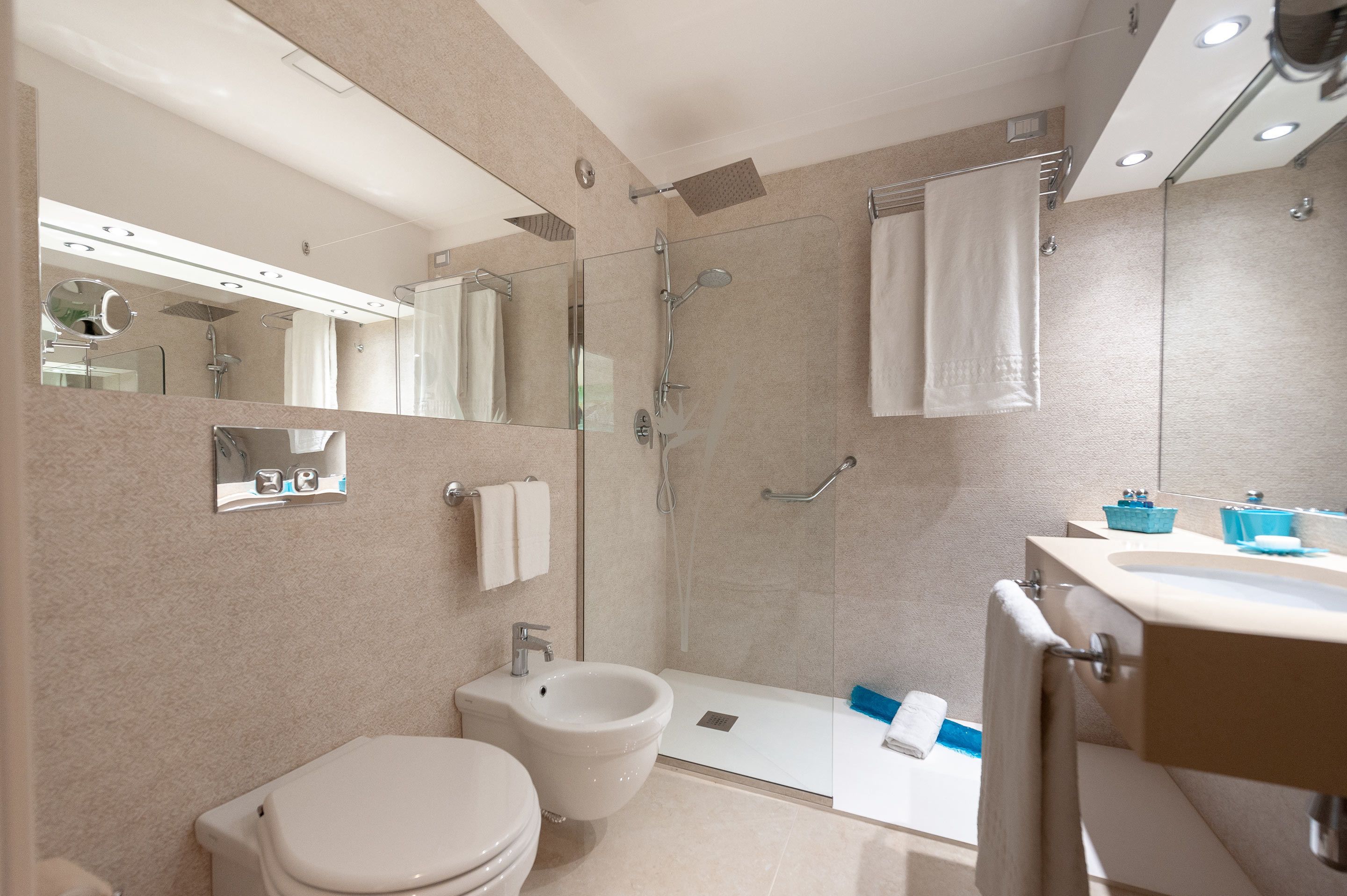 Un baño moderno con inodoro, bidé, cabina de ducha de vidrio y lavabo con espejo superior.