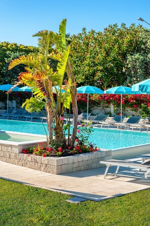 A pool area with lounge chairs and umbrellas, surrounded by lush greenery and flowering plants. - Acacia Palace (Ragusa)