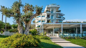 Un hotel moderno de varios pisos con fachada de vidrio, zona de estar al aire libre y abundante vegetación.