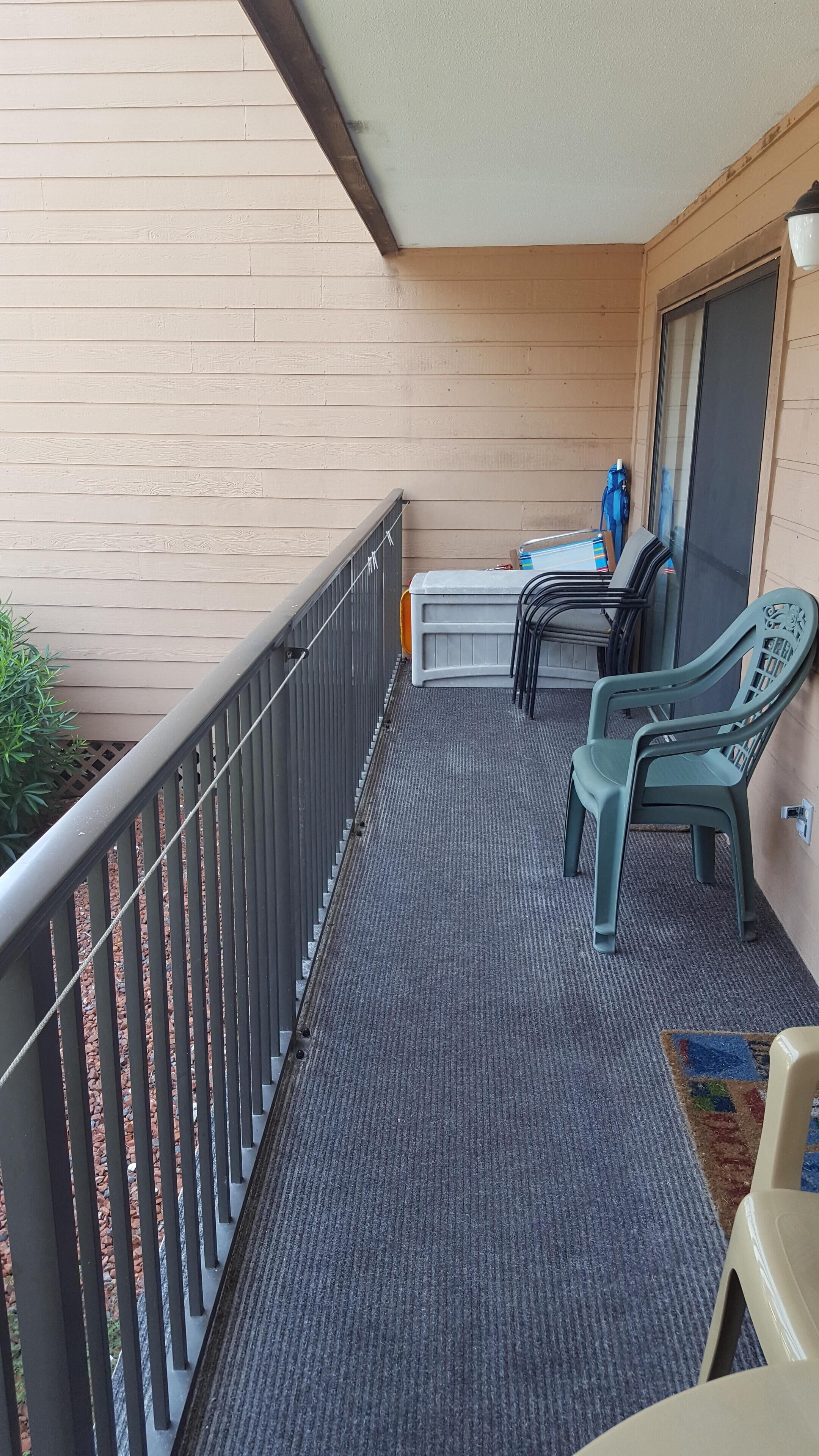 Ein Balkon mit grauem Teppich, einem Metallgeländer und zwei grünen Plastikstühlen.