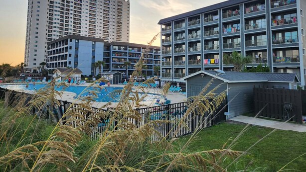 Um hotel com vários andares, piscina e área cercada com espreguiçadeiras.