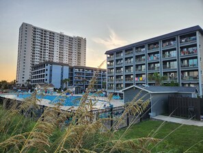 Un hotel con varios pisos, piscina y un área vallada con sillas de descanso.