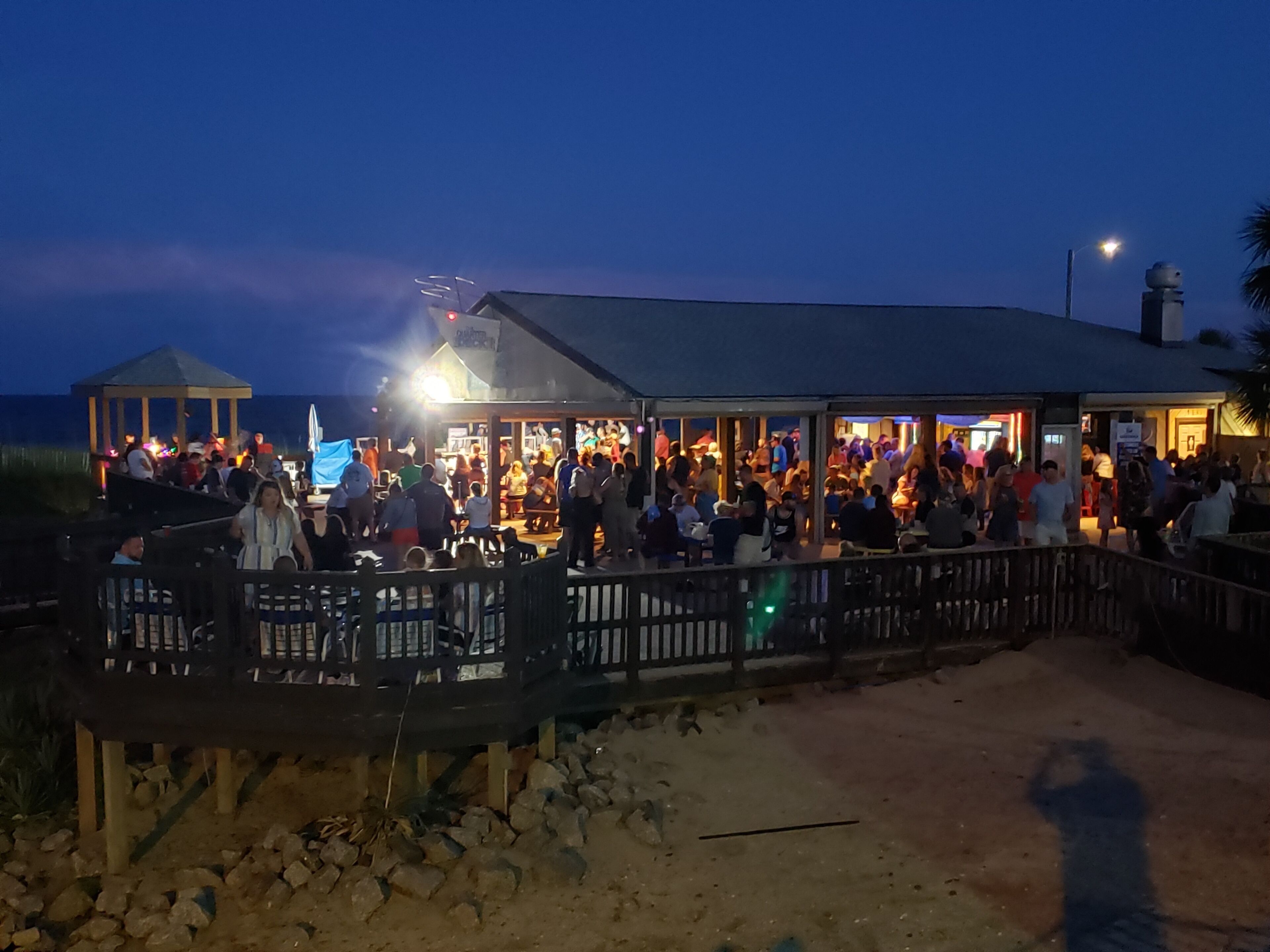 A crowded outdoor bar area with a covered seating area and a gazebo.