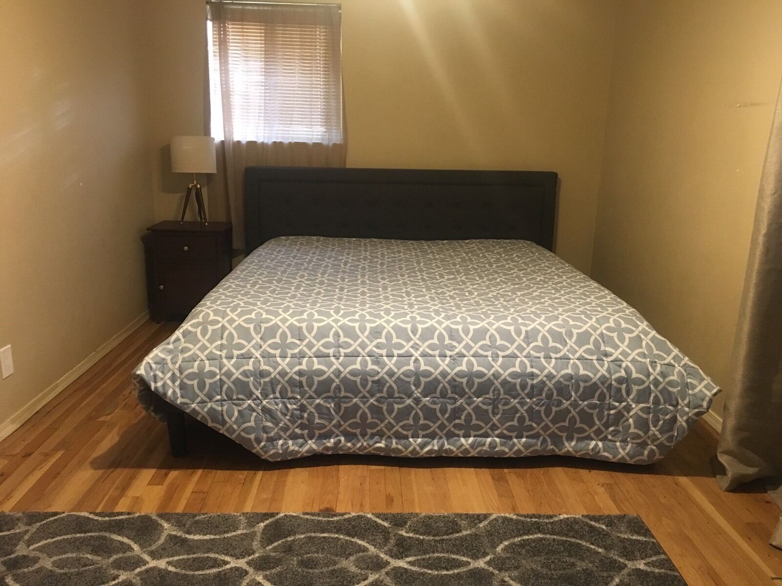 A bedroom with a bed, a nightstand, a lamp, and a window with blinds.