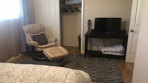 Une chambre à coucher avec un lit, un fauteuil massant, un téléviseur posé sur un meuble et une petite table avec une couverture.