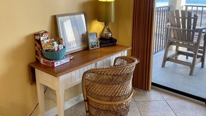 Een kamer met een bureau, een rieten stoel, een lamp en uitzicht op de oceaan.