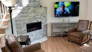 A living room with a stone fireplace, leather chairs, a flat-screen TV, and a staircase. - Beautiful Townhome Near Glacier Park!! (Columbia Falls)