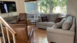 A living room with a brown leather sofa, a grey sofa with patterned cushions, a glass coffee table, and a television mounted on the wall. - Beautiful Townhome Near Glacier Park!! (Columbia Falls)