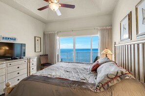 Ein Schlafzimmer mit Bett, Fernseher, Deckenventilator, Fenster mit Meerblick und einem Schild mit der Aufschrift 'BEACH'.
