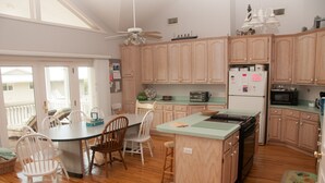 A kitchen with wooden cabinets, a central island, a dining table with chairs, and a ceiling fan. - Relax by the Sea! Wide Beach! Beautiful view from porch. (Fripp Island)