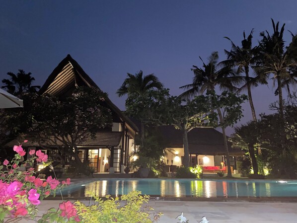 A resort with a swimming pool, palm trees, and a building with a thatched roof.