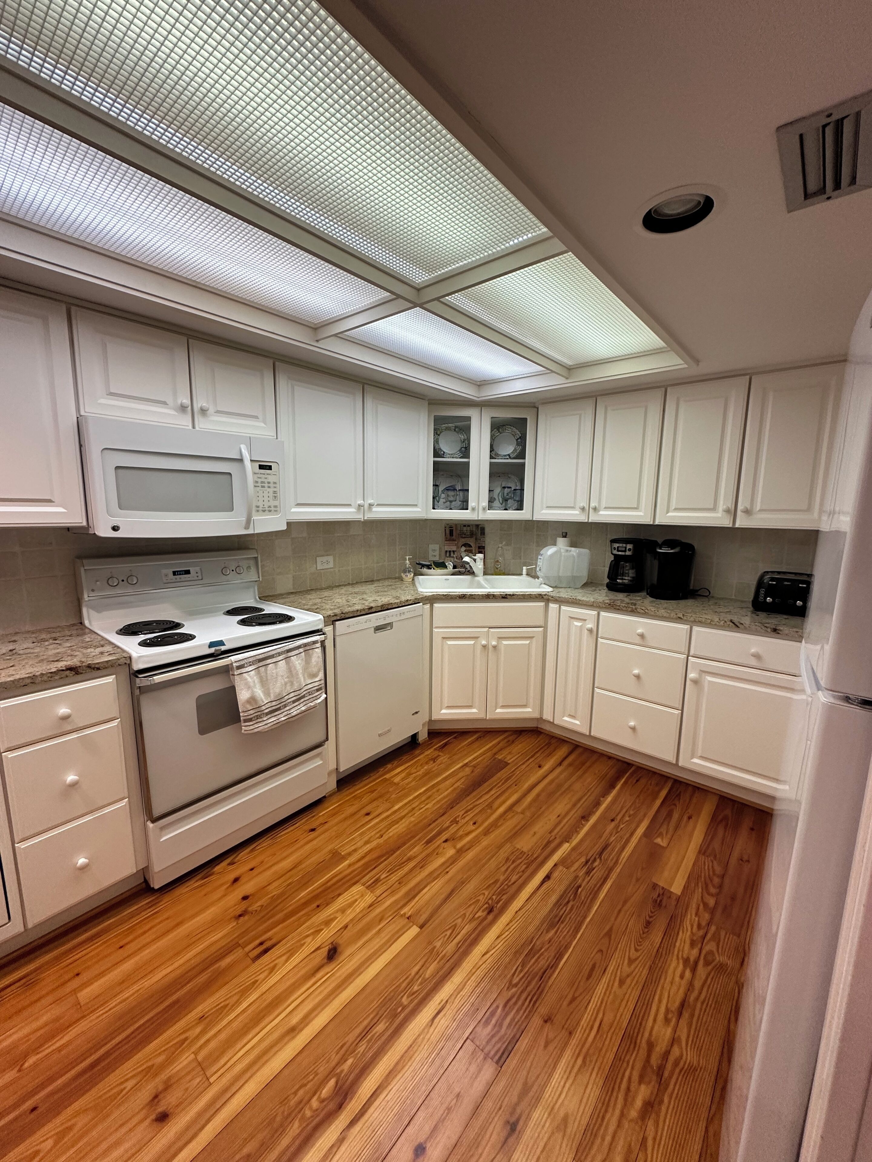 Une cuisine avec des meubles blancs, un four à micro-ondes, une cuisinière et un plancher en bois.