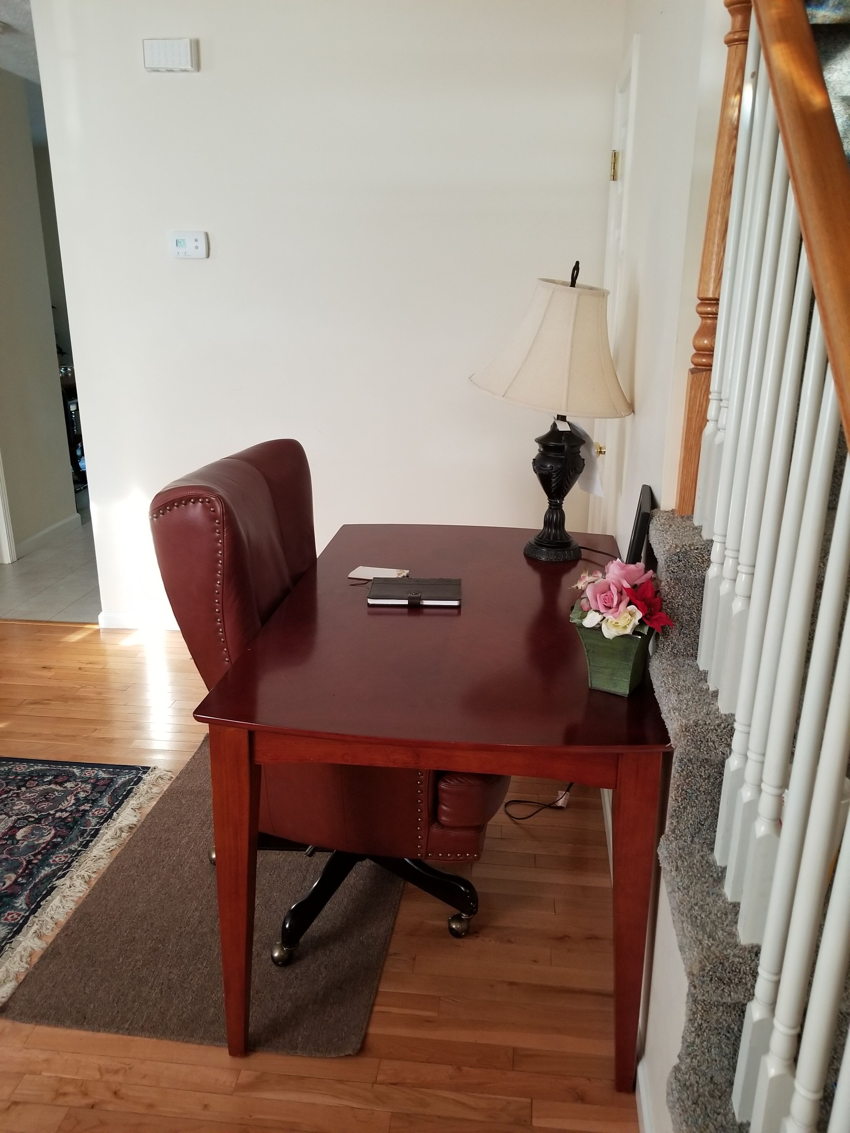 Une table de salle à manger en bois, agrémentée d’une lampe noire et d’un petit arrangement floral.