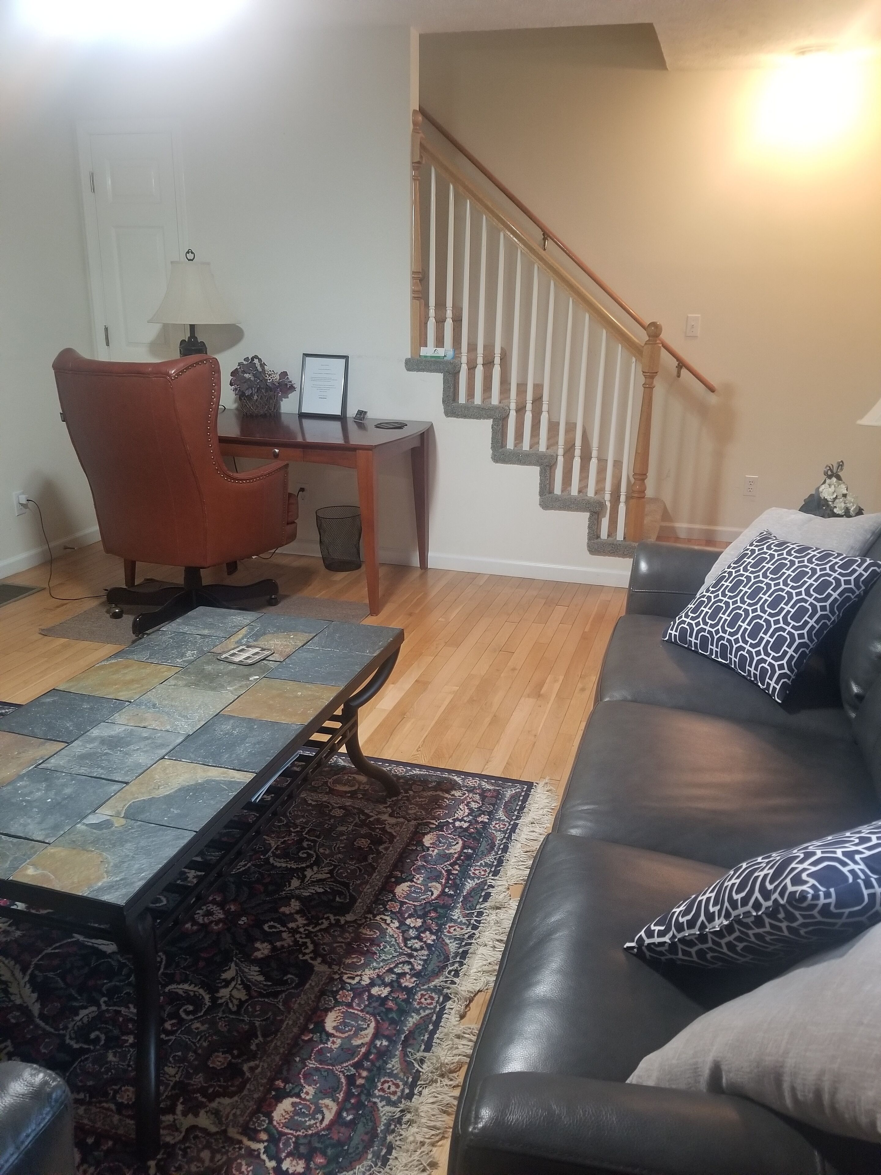 Un salon avec un canapé en cuir noir, un tapis à motifs, une table basse en bois et un escalier avec des rampes en bois.