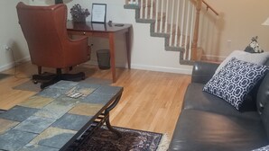 Un salon avec un canapé en cuir noir, un tapis à motifs, une table basse en bois et un escalier avec des rampes en bois.
