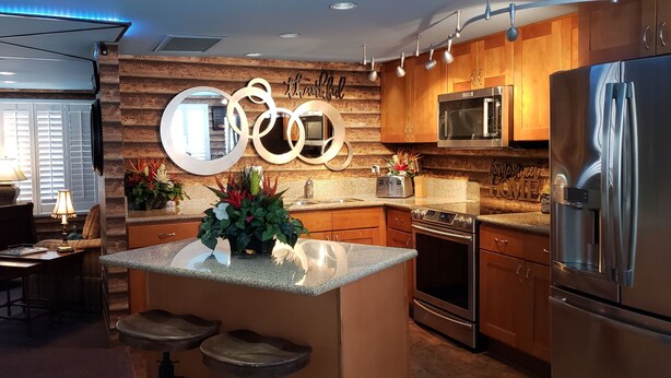 A modern kitchen with wooden cabinets, stainless steel appliances, a central island with stools, and decorative mirrors.